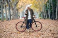 Beautiful young woman sending messages with her smart phone while cycling through the park in autumn Royalty Free Stock Photo