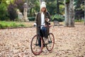 Beautiful young woman sending messages with her smart phone while cycling through the park in autumn Royalty Free Stock Photo