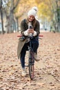 Beautiful young woman sending messages with her smart phone while cycling through the park in autumn Royalty Free Stock Photo