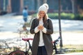 Beautiful young woman sending messages with her smart phone while cycling through the park in autumn Royalty Free Stock Photo