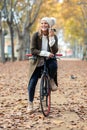 Beautiful young woman sending voice audio message with her smart phone while cycling through the park in autumn Royalty Free Stock Photo