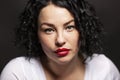 Beautiful young woman with a serious expression. Brunette with curly hair. Close-up. Black background