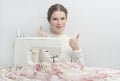 Beautiful young woman sews a curtain on a sewing machine and shows her thumb Royalty Free Stock Photo
