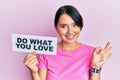 Beautiful young woman with short hair holding paper with do what you love text doing ok sign with fingers, smiling friendly