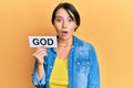 Beautiful young woman with short hair holding paper with god word scared and amazed with open mouth for surprise, disbelief face Royalty Free Stock Photo