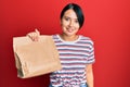 Beautiful young woman with short hair holding take away paper bag looking positive and happy standing and smiling with a confident Royalty Free Stock Photo
