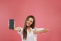 Beautiful young woman shoving smartphone with copy space and looking at camera while standing against  pink background. Take a loo Royalty Free Stock Photo