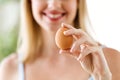 Beautiful young woman showing brown chiken egg at home.