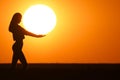 Beautiful young woman silhouette at sunset. The girl is holding the big day in her hands.