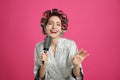 Beautiful young woman in silk bathrobe with hair curlers singing into hairbrush on pink background Royalty Free Stock Photo