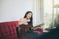 Beautiful young woman singing and playing guitar while sitting on couch in living room at home Royalty Free Stock Photo