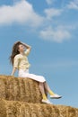 Beautiful young woman sits on haystack on blue sky background. Relaxing on summer field with hay stacks. Summer vacation Royalty Free Stock Photo