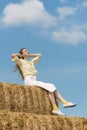 Beautiful young woman sits on haystack. Relaxing on summer field with hay stacks. Summer vacation Royalty Free Stock Photo