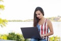 The beautiful young woman sits in the park near river with the laptop. Royalty Free Stock Photo