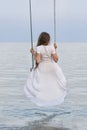 Beautiful young woman sits on rope swing on sea background. Vertical frame. Back view Royalty Free Stock Photo