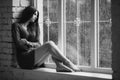 Beautiful young woman sitting alone close to window with rain drops. and sad girl. Concept of loneliness. Black Royalty Free Stock Photo