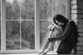 Beautiful young woman sitting alone near window with rain drops. and sad girl with long slim legs. Concept of Royalty Free Stock Photo