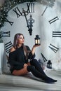 Beautiful young woman sitting on the background of a large clock Christmas decor, holding a flashlight, waiting for the holiday