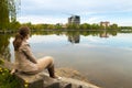 Beautiful young woman sitting on the bank of big lake with modern city skyline of buildings under construction Royalty Free Stock Photo