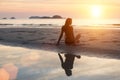 Beautiful young woman sitting on the beach in the setting sun Royalty Free Stock Photo