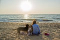 Beautiful young woman sitting on the beach with two dogs playing around during sunset Royalty Free Stock Photo