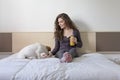 beautiful young woman sitting on bed with her cute small dog besides. Home, indoors and lifestyle. She is drinking orange juice. Royalty Free Stock Photo