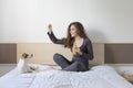 beautiful young woman sitting on bed with her cute small dog besides. Home, indoors and lifestyle. She is drinking orange juice.