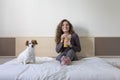 beautiful young woman sitting on bed with her cute small dog besides. Home, indoors and lifestyle. She is drinking orange juice. Royalty Free Stock Photo