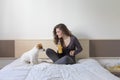 beautiful young woman sitting on bed with her cute small dog besides. Home, indoors and lifestyle. She is drinking orange juice. Royalty Free Stock Photo