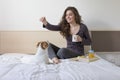 Beautiful young woman sitting on bed with her cute small dog besides. Home, indoors and lifestyle. She is having breakfast on bed Royalty Free Stock Photo