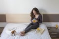 beautiful young woman sitting on bed with her cute small dog besides. Home, indoors and lifestyle. She is having breakfast on bed Royalty Free Stock Photo