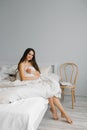 Beautiful young woman is sitting on the bed wrapped in a blanket. Portrait of a smiling lady posing in a bright home apartment. Royalty Free Stock Photo