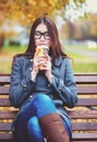 Beautiful young woman sitting on a bench drinking coffee or hot tea in the spring autumn coat enjoying in park outdoor