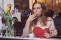 Beautiful young woman sitting in coffee shop, looking out of the window, drining coffee and eating dessert