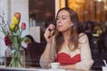 Beautiful young woman sitting in coffee shop near the window,drining coffee and eating dessert