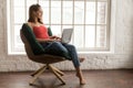 Beautiful young woman sitting in comfortable chair and using laptop Royalty Free Stock Photo