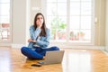 Beautiful young woman sitting on the floor with crossed legs using laptop looking stressed and nervous with hands on mouth biting