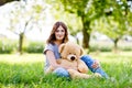 Beautiful young woman sitting on green grass in summer. Lady with long hairs holding huge teddy bear Royalty Free Stock Photo