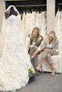 Beautiful young woman sitting with mother while looking at wedding gown in bridal store