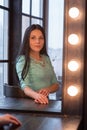 Beautiful young woman sitting near dressing table at home. Beautiful brunette in a dress Royalty Free Stock Photo