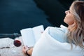 beautiful young woman is sitting on pier with glass of red wine and book having great time on vacation , happy evening. Royalty Free Stock Photo