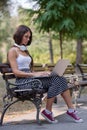 Beautiful young woman sitting in public park working on laptop computer Royalty Free Stock Photo