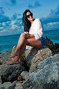 Beautiful young woman sitting on a rock by the ocean Royalty Free Stock Photo