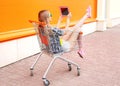 Beautiful young woman sitting in shopping trolley cart over colorful orange Royalty Free Stock Photo