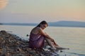 Beautiful young woman sitting on shore of lake in summer dress at sunset. Portrait of a romantic wet girl at sunset, warm sun, Royalty Free Stock Photo