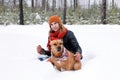 Beautiful young woman is sitting on a snow and playing with her American Staffordshire Terrier dog in winter coniferous forest Royalty Free Stock Photo