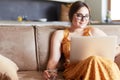 Beautiful young woman sitting on a sofa and working on a laptop Royalty Free Stock Photo