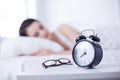 Beautiful young woman sleeping while lying in bed comfortably and blissfully on the background of alarm clock