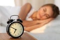 Beautiful young woman sleeping and smiling while lying in bed comfortably and blissfully on the background of alarm Royalty Free Stock Photo