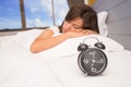 Beautiful young woman sleeping and smiling while lying in bed comfortably and blissfully on the background of alarm clock Royalty Free Stock Photo